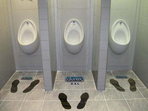 In einer Herrentoilette weisen Fußabdrücke auf dem Boden zu Urinalen mit Durex-Werbung.