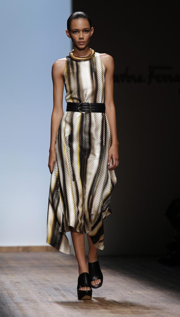 Eine Frau präsentiert ein ärmelloses Kleid mit Streifen und schwarzem Gürtel auf dem Laufsteg.