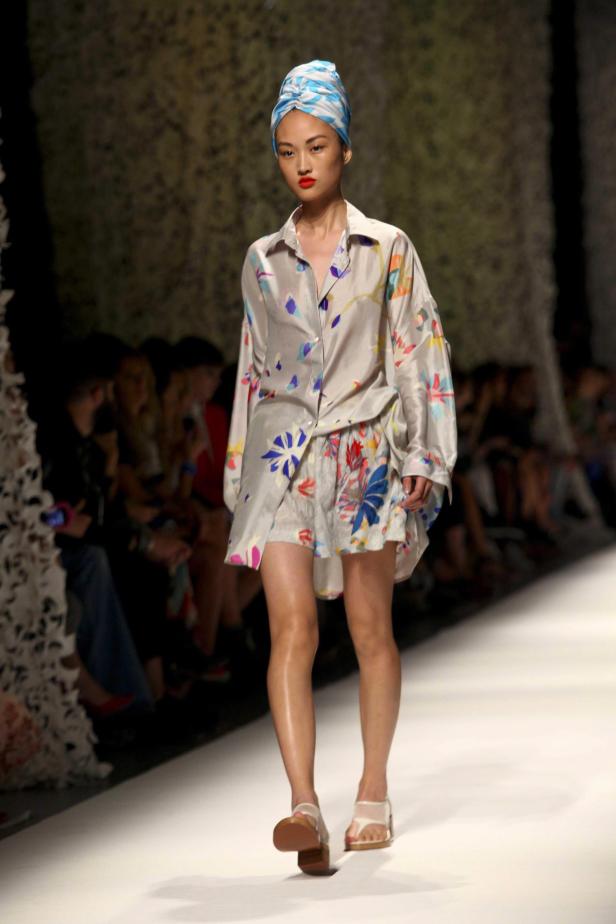 Ein Model mit einem blau-weiß gemusterten Turban auf dem Laufsteg präsentiert ein farbenfrohes Outfit.