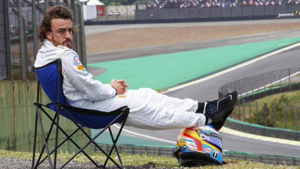Fernando Alonso sitzt in einem Stuhl und ruht sich auf seinem Helm aus.