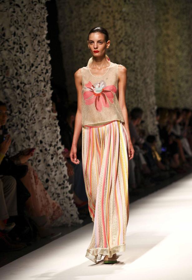 Eine Frau präsentiert ein ärmelloses Oberteil mit Blumenmuster und einen langen, gestreiften Rock auf dem Laufsteg.