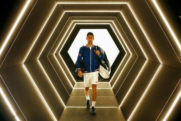 Novak Đoković betritt einen beleuchteten Tunnel mit Tennistasche.
