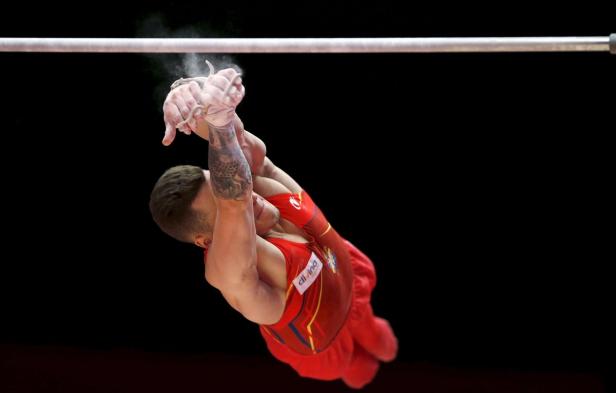 Ein Turner in roter Sportkleidung schwingt an einem Reck mit Magnesium an den Händen.