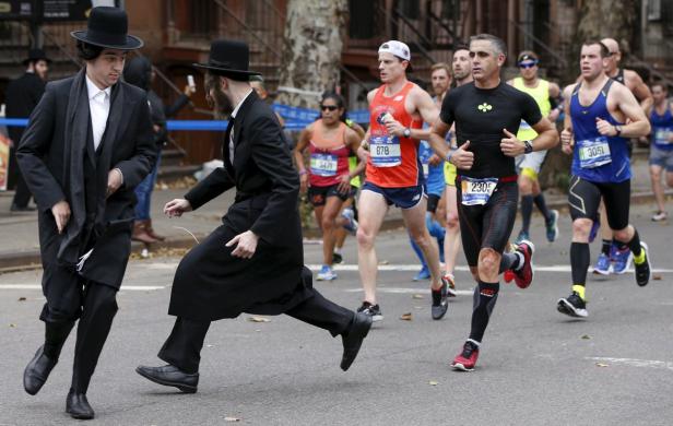 Zwei orthodoxe Juden überqueren eine Straße, während ein Marathon stattfindet.