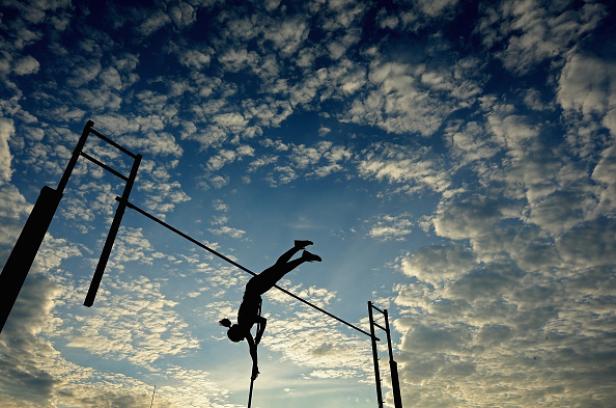 Die Silhouette einer Stabhochspringerin vor einem Himmel mit Wolken.