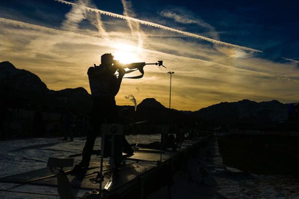Ein Biathlet zielt bei Sonnenuntergang mit seinem Gewehr auf eine Zielscheibe.