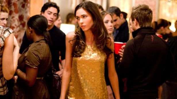 Eine Frau in einem goldenen Paillettenkleid steht auf einer Party.