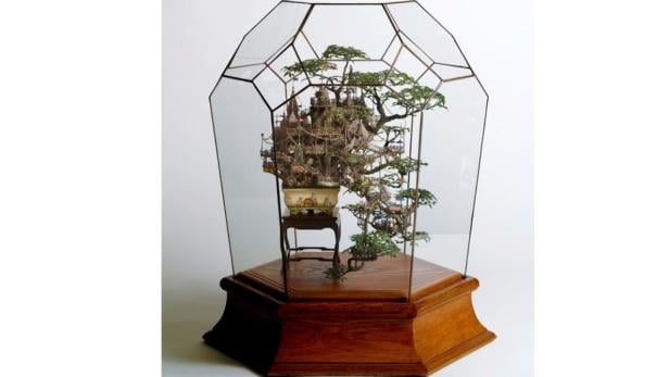 Ein Bonsai-Baum mit einem filigranen Miniaturhaus in einem gläsernen Terrarium.