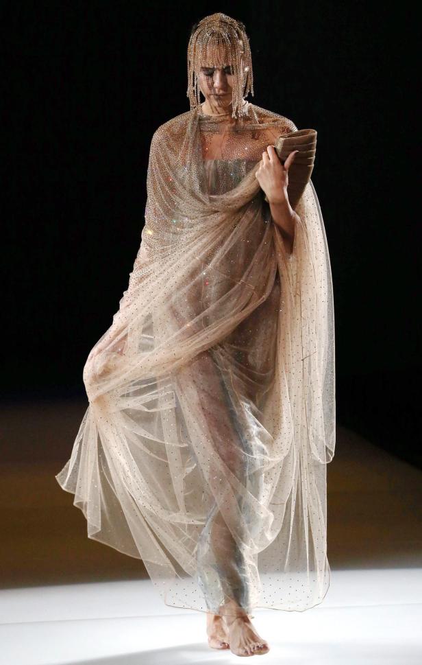 Ein Model präsentiert ein mit Pailletten besetztes Kleid und einen Kopfschmuck auf dem Laufsteg.