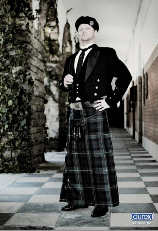 Ein Mann in traditioneller schottischer Kleidung, inklusive Kilt und Barett, posiert in einem Gang.
