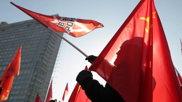 Eine Demonstration mit roten Fahnen und Hammer und Sichel vor einem Hochhaus.