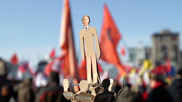 Eine Pappfigur von Putin steht auf einem Sockel vor einer Menge mit roten Fahnen.