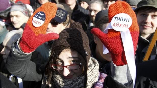 Eine Frau auf einer Demonstration hält Schilder an ihren Handschuhen hoch.