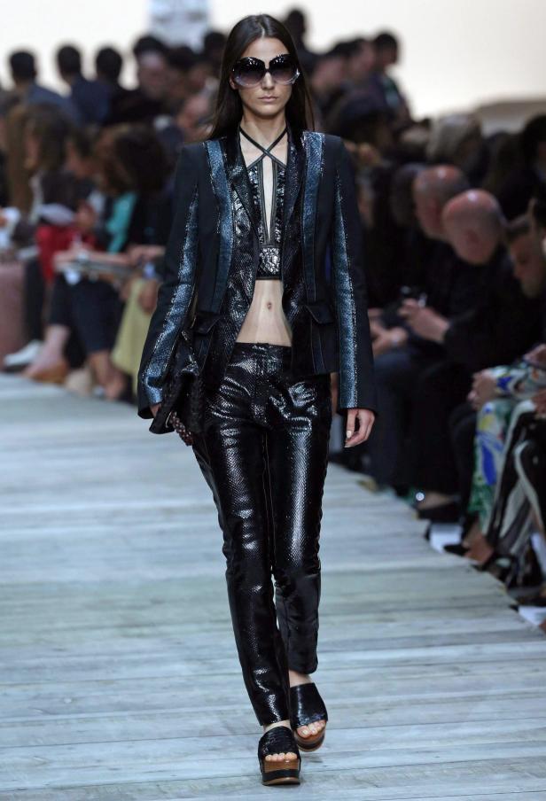 Eine Frau in einem glänzenden schwarzen Hosenanzug auf einem Laufsteg.