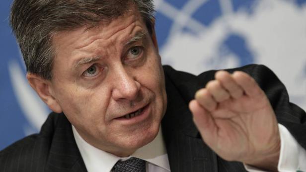 Ein Mann im Anzug gestikuliert vor einem blauen Hintergrund.