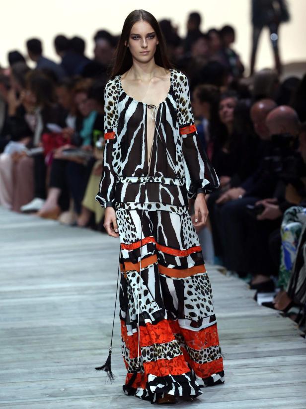 Eine Frau präsentiert ein langes, gemustertes Kleid auf einem Laufsteg.