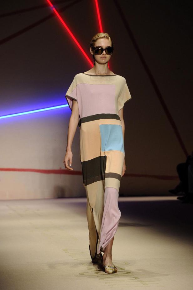 Eine Frau mit Sonnenbrille präsentiert ein farbenfrohes Kleid auf dem Laufsteg.