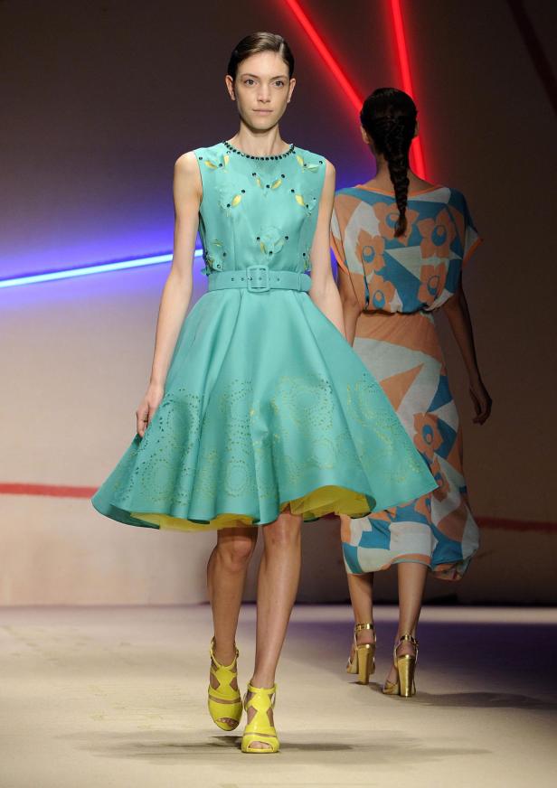 Eine Frau präsentiert ein türkisfarbenes Kleid mit gelben Akzenten auf dem Laufsteg.