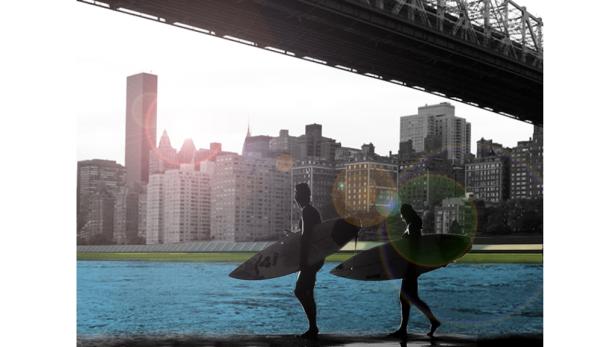 Zwei Surfer mit Surfbrettern vor der Skyline von New York City.