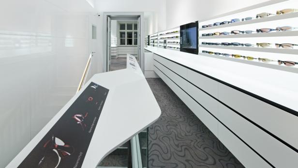 Innenansicht eines modernen Optikergeschäfts mit Brillen auf Regalen.