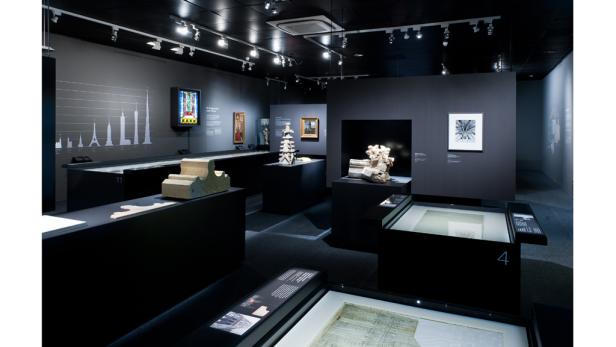 Innenansicht einer Ausstellung mit Architekturmodellen und Zeichnungen auf schwarzen Podesten.