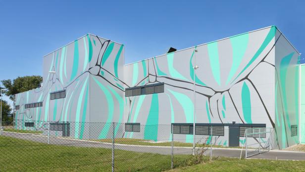 Ein großes, graues Gebäude mit türkisfarbenen und schwarzen Verzierungen an der Fassade.