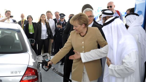 Angela Merkel tankt ein Auto, umgeben von einer Gruppe von Menschen.