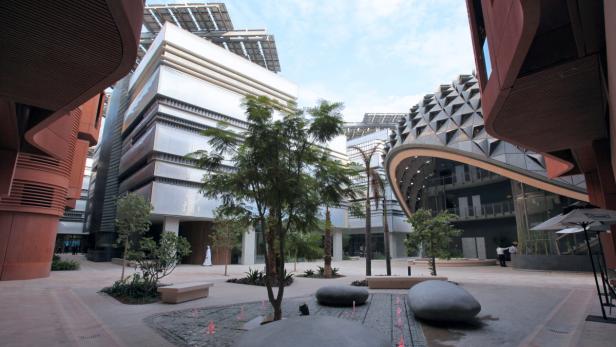 Blick auf einen Platz mit moderner Architektur und Bäumen in Masdar City, Abu Dhabi.