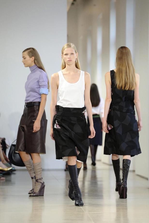 Drei Models präsentieren Röcke und Stiefel auf einem Laufsteg.