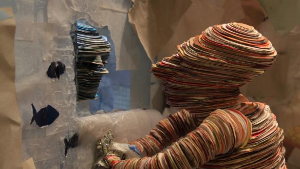 Eine Skulptur aus Papier zeigt ein Gesicht im Profil und eine sitzende Figur.