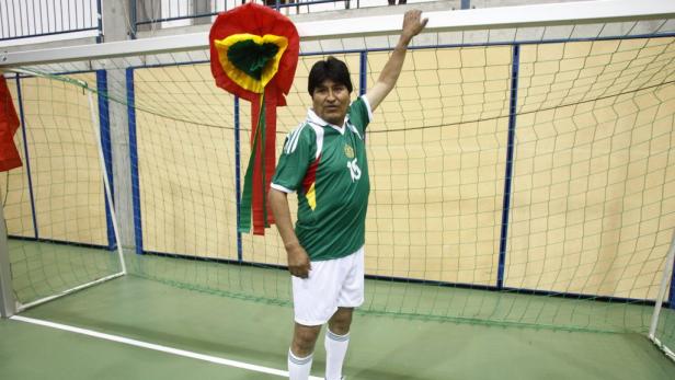 Evo Morales in Fußballkleidung vor einem Fußballtor mit bolivianischer Dekoration.