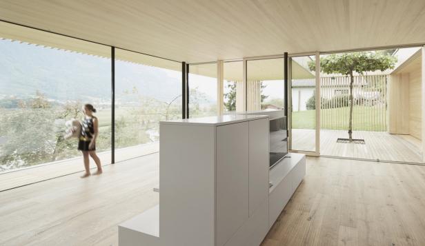 Ein Mädchen steht in einem hellen, modernen Wohnzimmer mit Blick auf eine grüne Landschaft.
