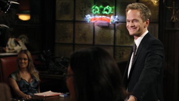 Neil Patrick Harris lächelt in einem Anzug vor einer Bar-Kulisse.