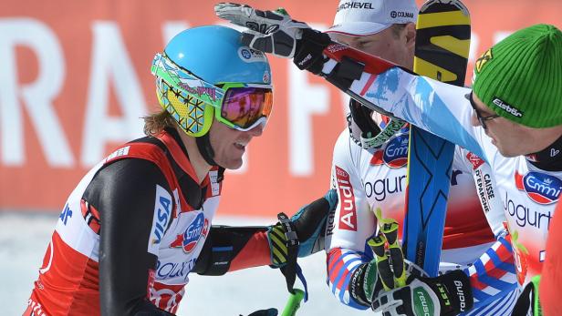 Ein Skirennläufer mit blauem Helm wird von zwei Betreuern beglückwünscht.