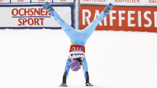 Eine Skirennläuferin macht einen Handstand auf der Skipiste.