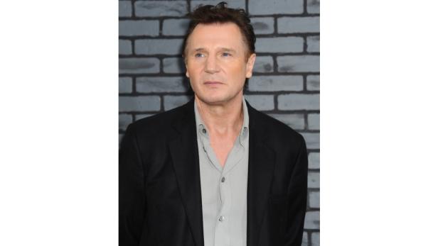Porträt von Liam Neeson vor einer grauen Ziegelwand.