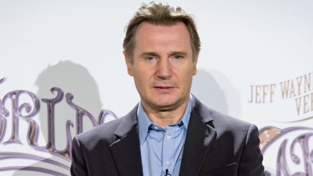 Liam Neeson posiert vor einem Werbeplakat für „Jeff Wayne's The War of the Worlds“.