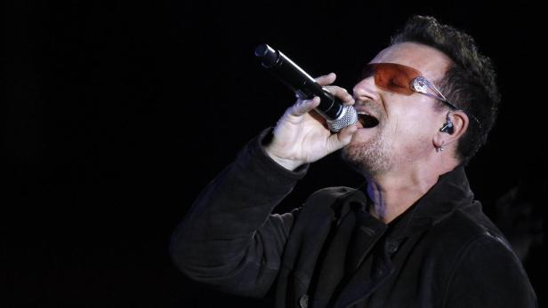 Bono, der Sänger von U2, singt mit Sonnenbrille in ein Mikrofon.