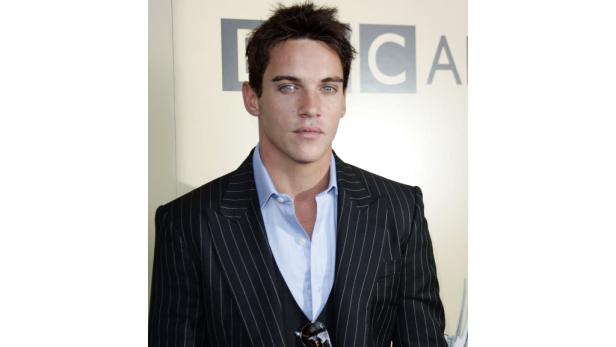 Ein Mann mit hellen Augen trägt einen Anzug mit Nadelstreifen.