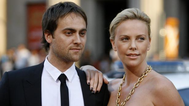 Charlize Theron mit einer Hand auf der Schulter eines Mannes in einem Anzug.