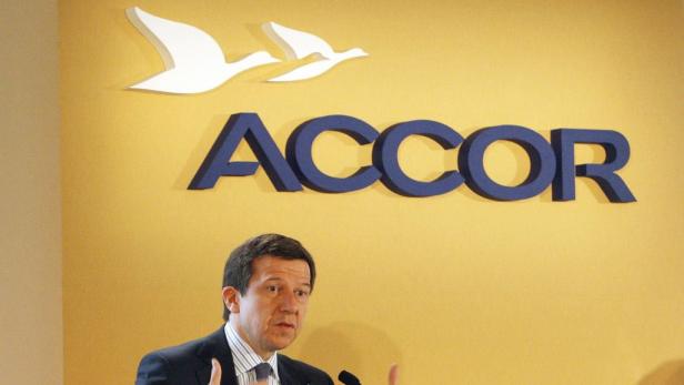 Ein Mann spricht vor dem Accor-Logo mit zwei stilisierten Vögeln an einer gelben Wand.