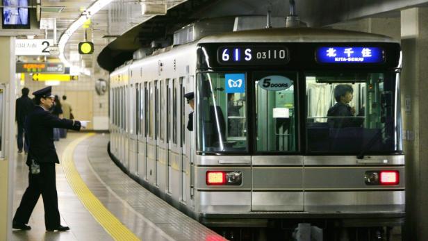 Ein Bahnangestellter gibt einem einfahrenden Zug in der Station Kita-Senju ein Signal.