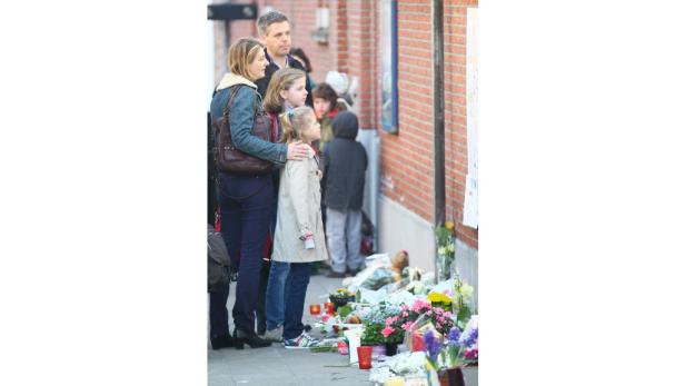 Eine Familie betrachtet eine Gedenkstätte mit Blumen und Kerzen an einer Backsteinmauer.