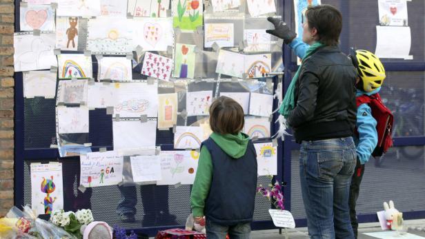 Eine Frau und zwei Kinder betrachten eine Wand mit Kinderzeichnungen und Blumen.