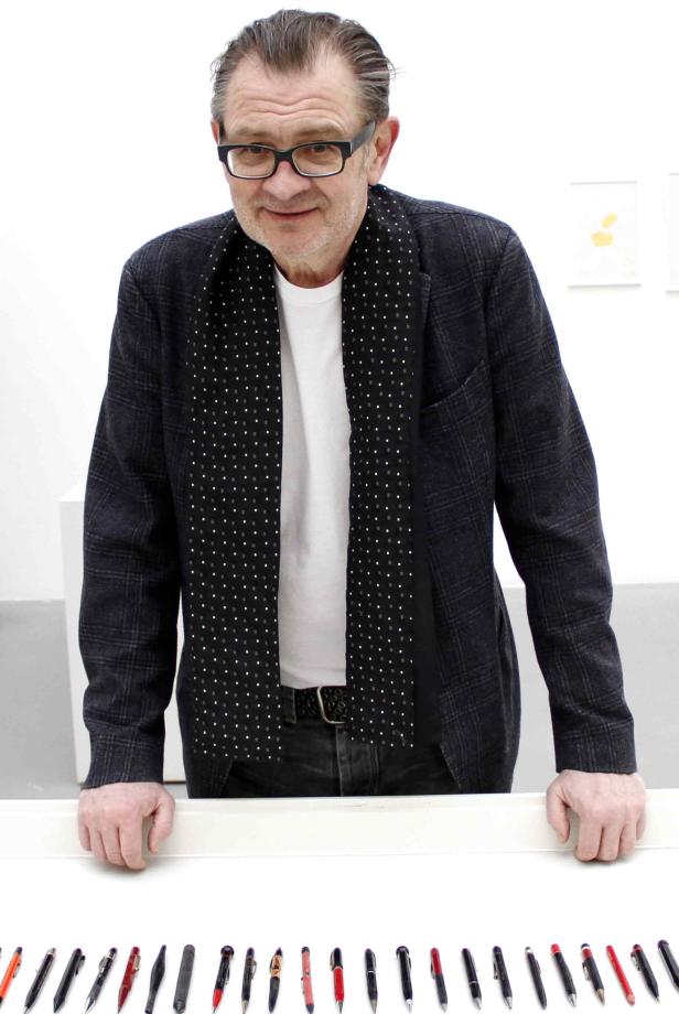 Ein Mann mit Brille betrachtet eine Reihe von Stiften auf einem Tisch.