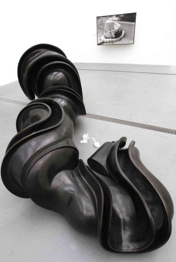 Eine gewundene, dunkle Skulptur liegt auf dem Boden einer Galerie.