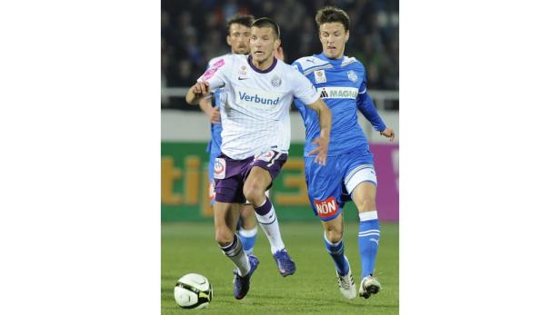 Zwei Fußballspieler kämpfen um den Ball auf dem Spielfeld.