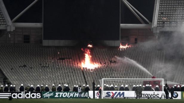 Auf den Rängen eines Fußballstadions brennt es, während Sicherheitskräfte das Feuer löschen.