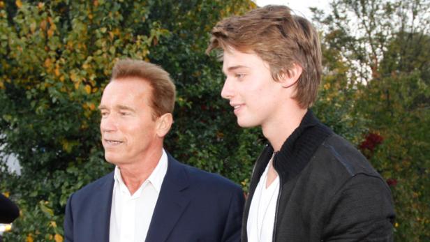 Arnold Schwarzenegger und Patrick Schwarzenegger posieren zusammen vor einem grünen Hintergrund.