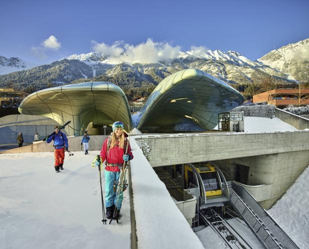Skifahrer verlassen die Hungerburgbahn in Innsbruck vor einer verschneiten Bergkulisse.